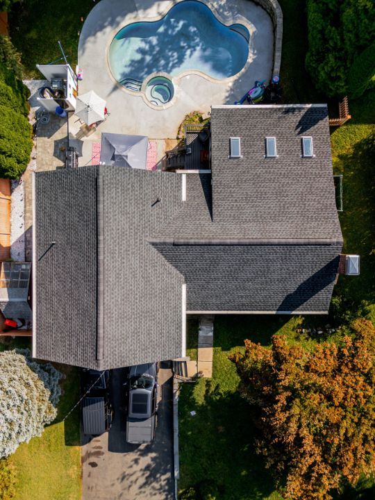 Overhead view of house with dark roof, driveway with car, and a backyard with pool.
