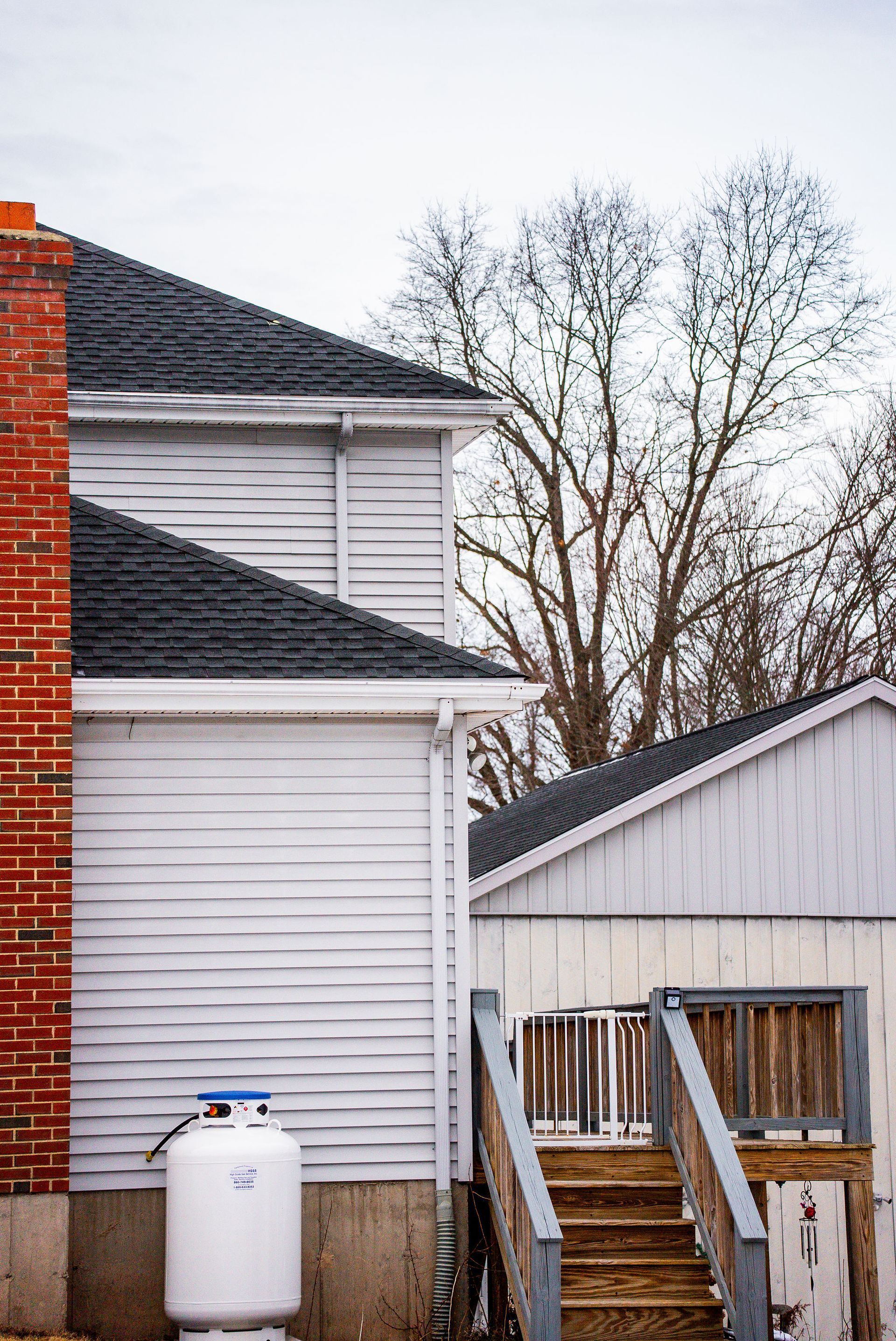 Buildings with a brick chimney, white siding, and outdoor stairs. A propane tank is in front.