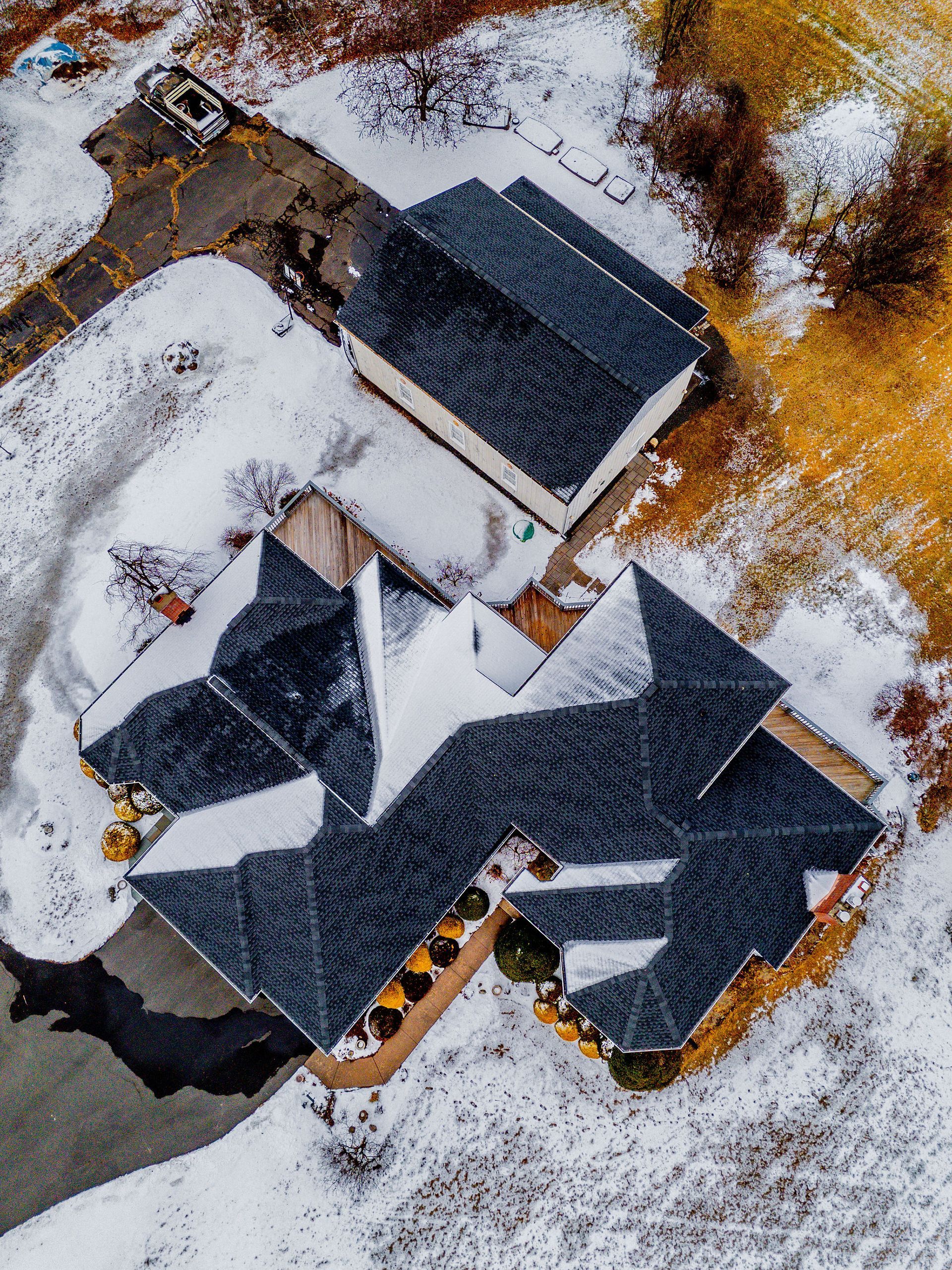 Aerial view of a house and detached garage covered in snow, on a snowy lot, with a driveway.