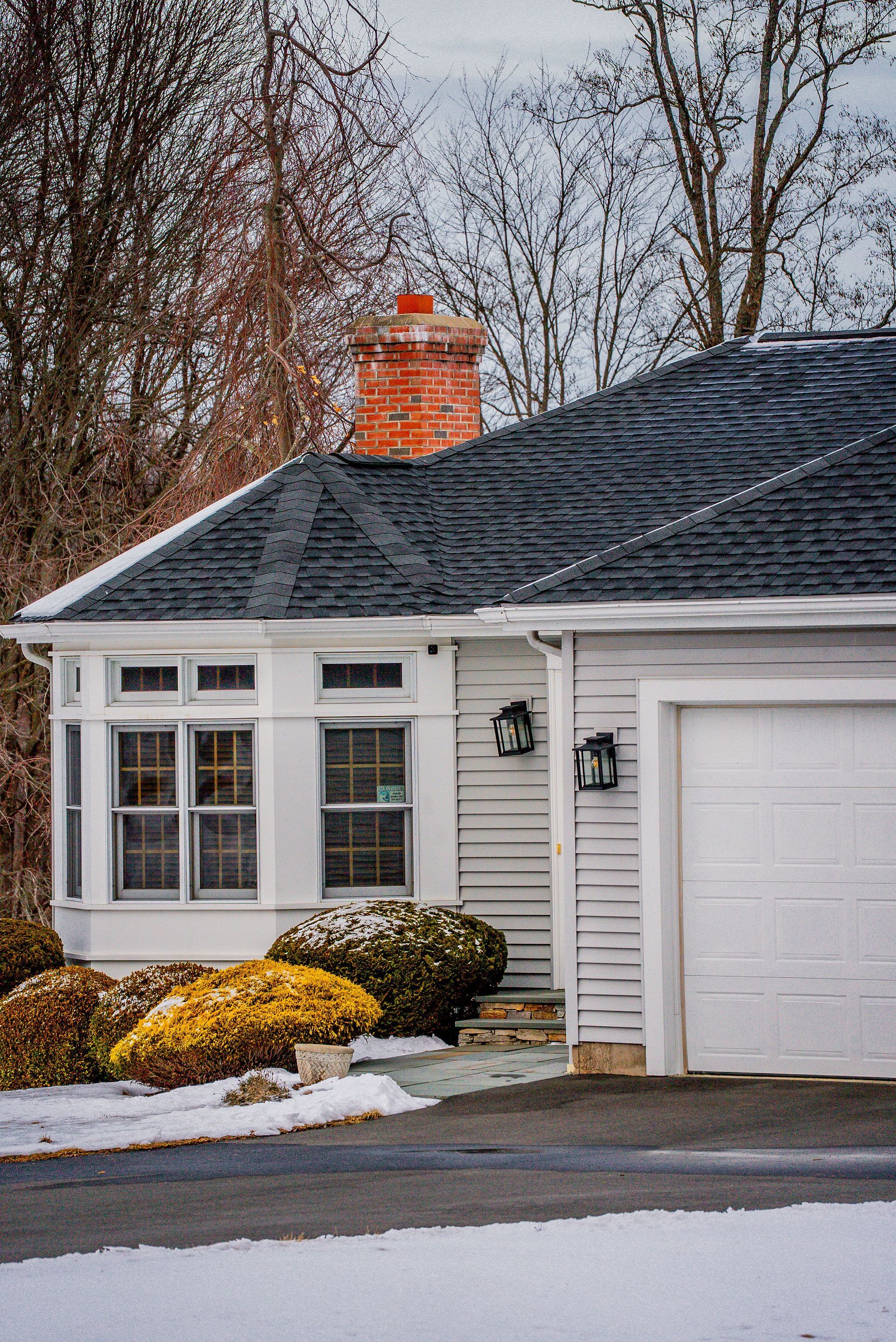 White house with dark roof and brick chimney in a snowy setting.