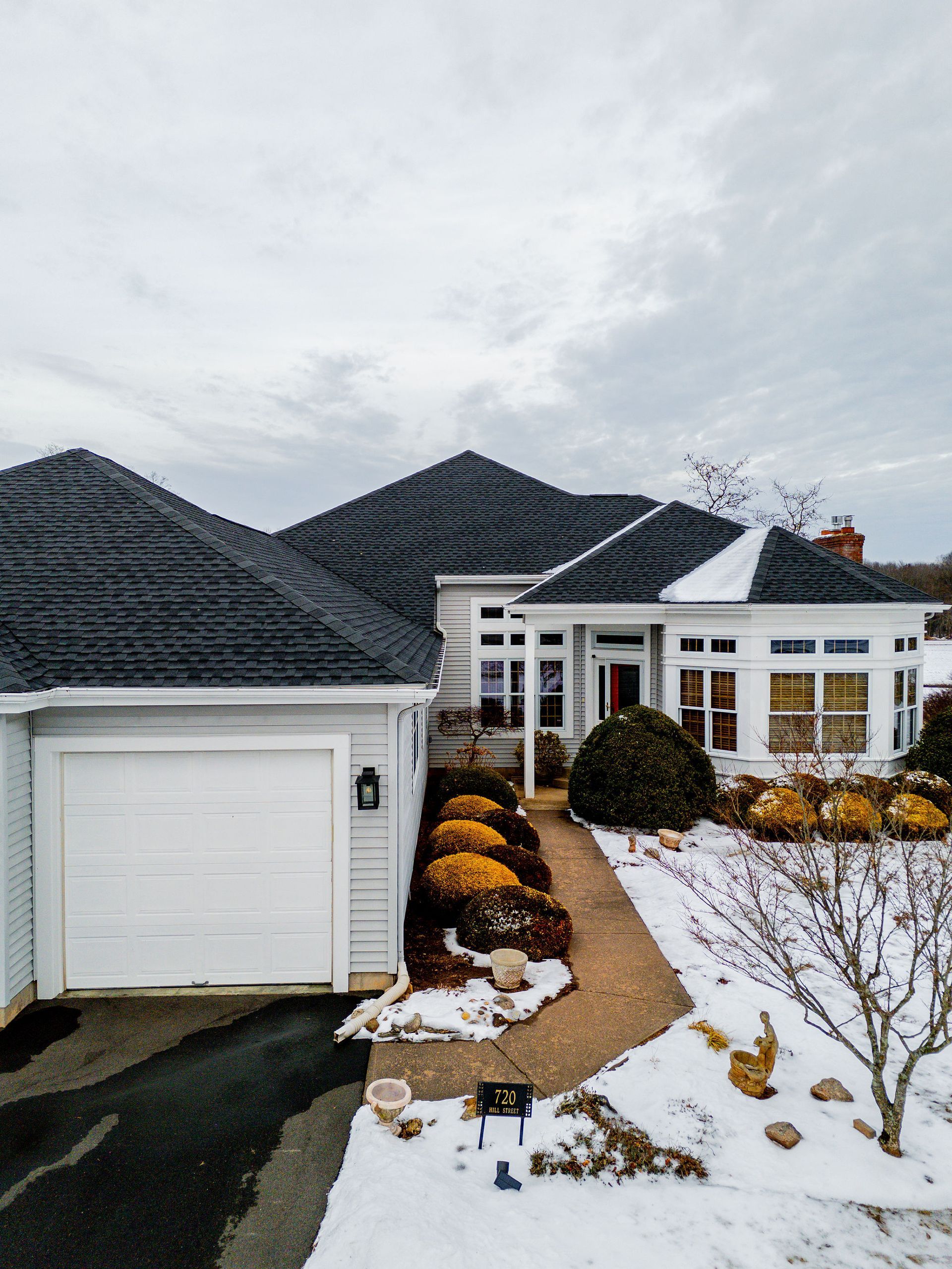 A light blue house with a dark gray roof, a white garage door, and a snow-covered pathway.