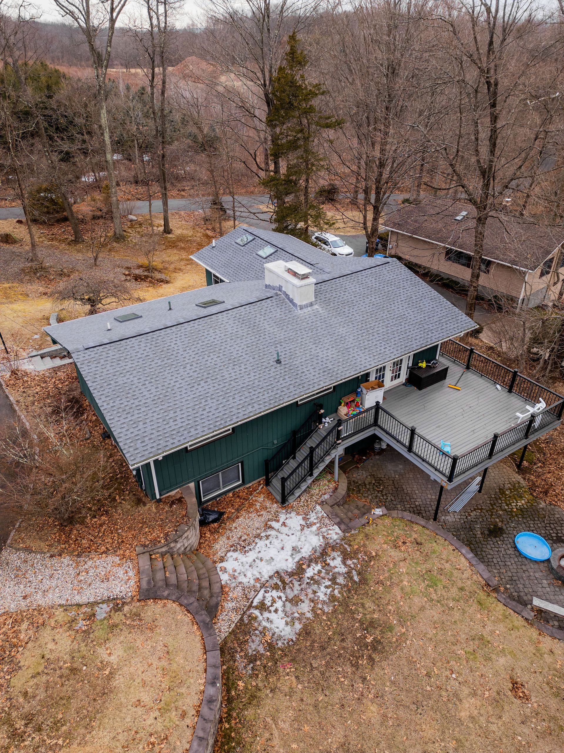 Green house with a deck in a wooded setting.