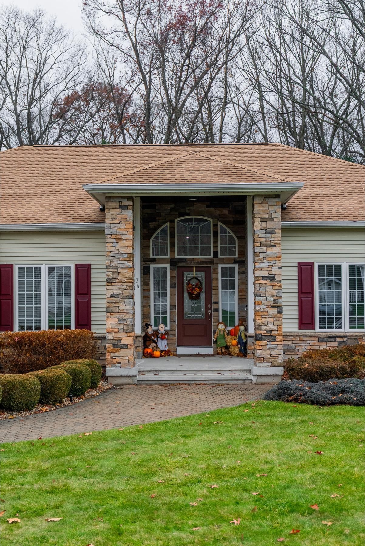 House with stone entrance, brown roof, and fall decorations on a cloudy day.