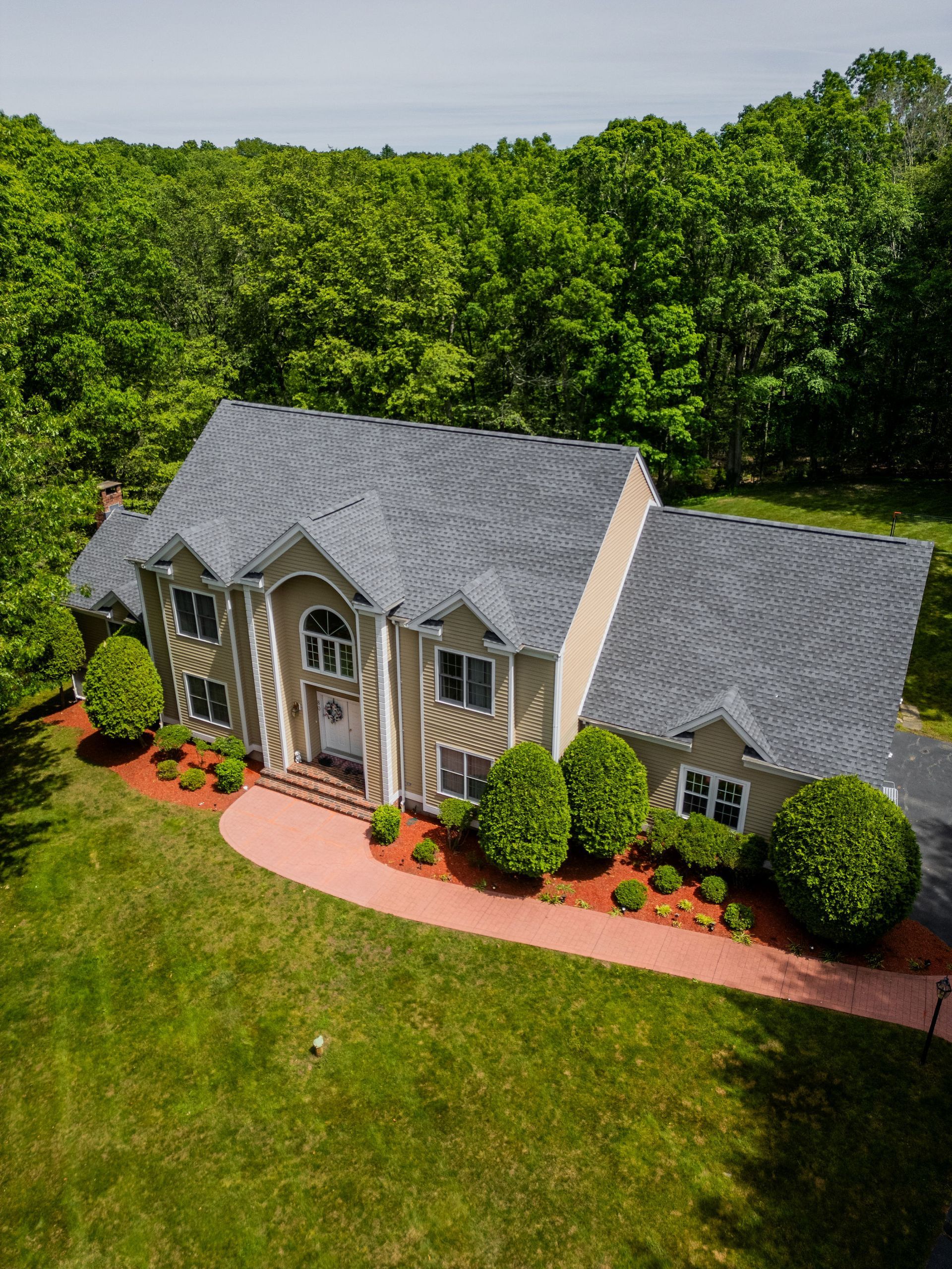 An aerial view of a large two-story house with gray roof, surrounded by green lawn and trees.