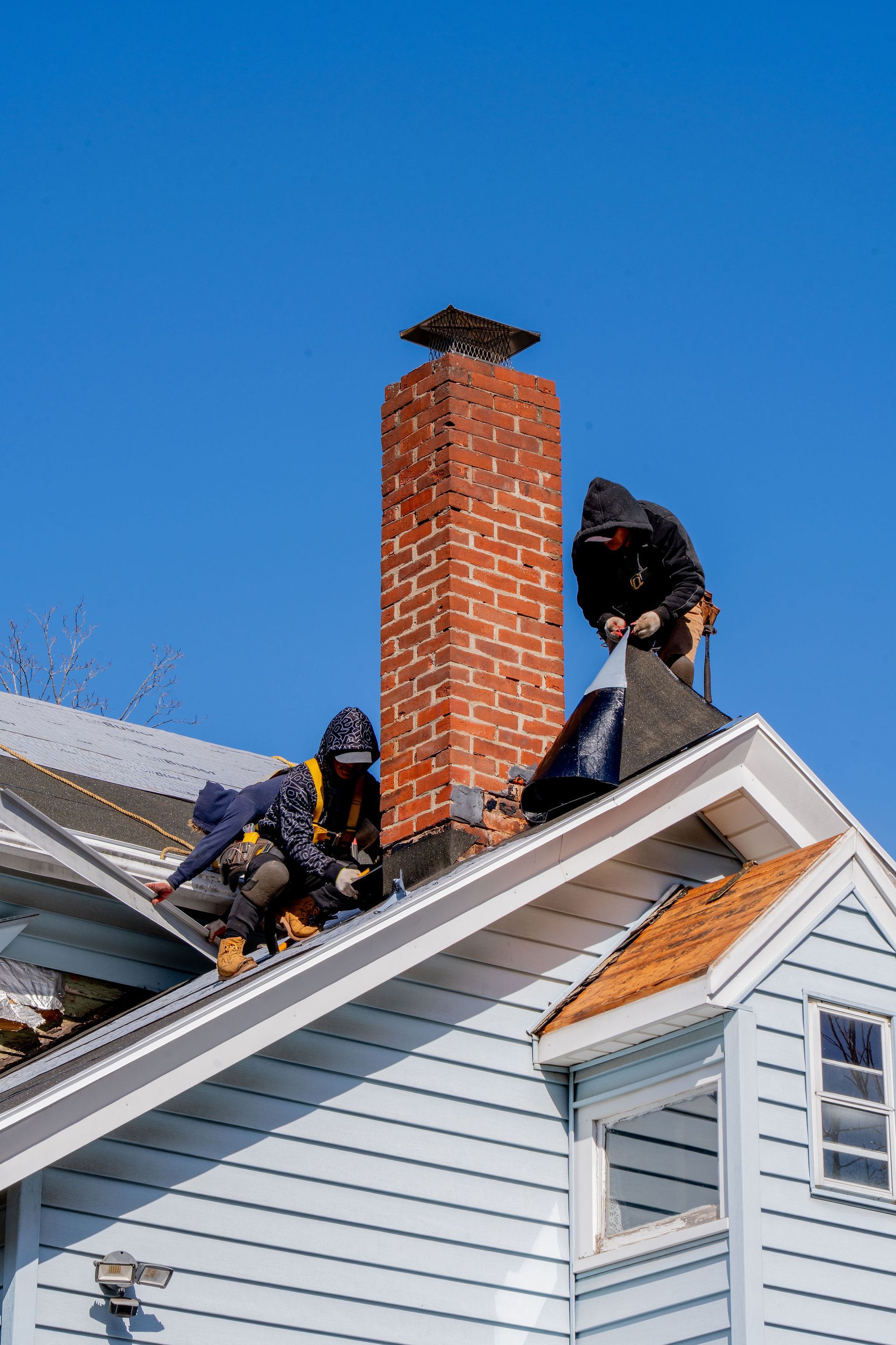 Two roofers working on a roof, blue house, brick chimney, sunny day.