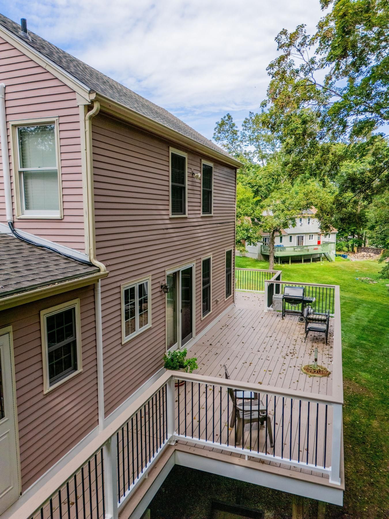 Two-story house with pink siding and a wooden deck overlooking a grassy backyard with trees.