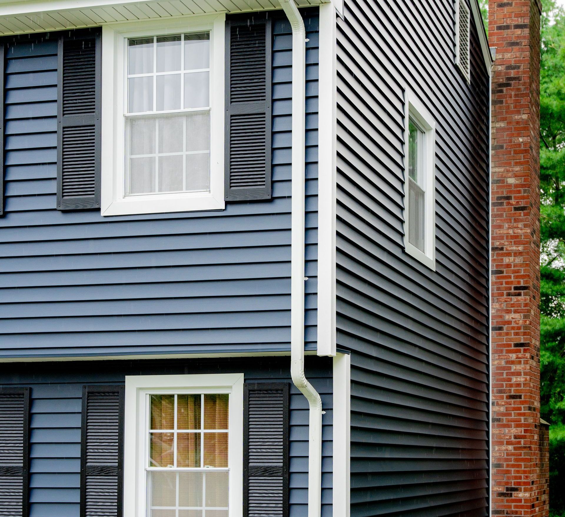 Two-story house with dark blue siding, white trim, black shutters, and a brick chimney.