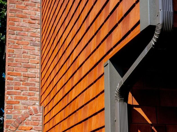 Red cedar shingle siding and brick chimney on a building, with dark gutter.