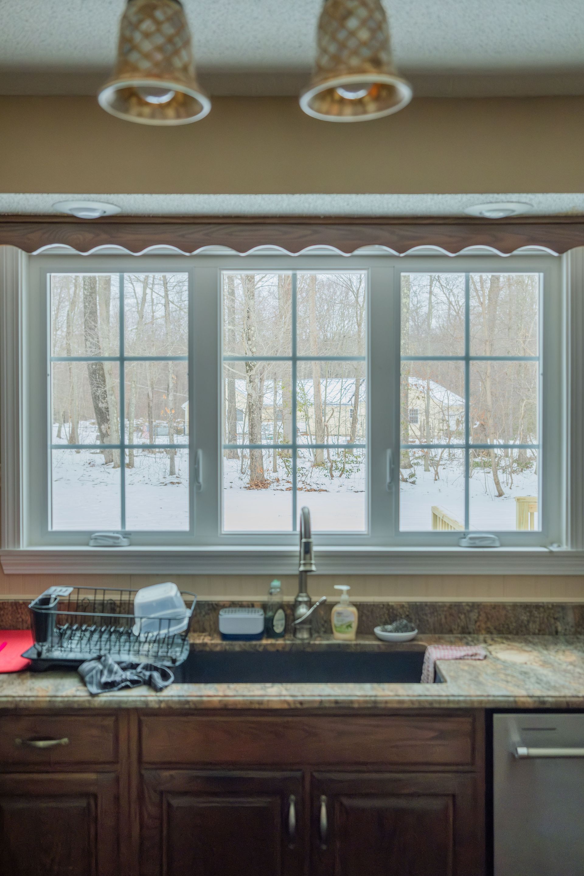 Kitchen sink with a window overlooking a snowy yard, dish rack, and dark cabinetry.