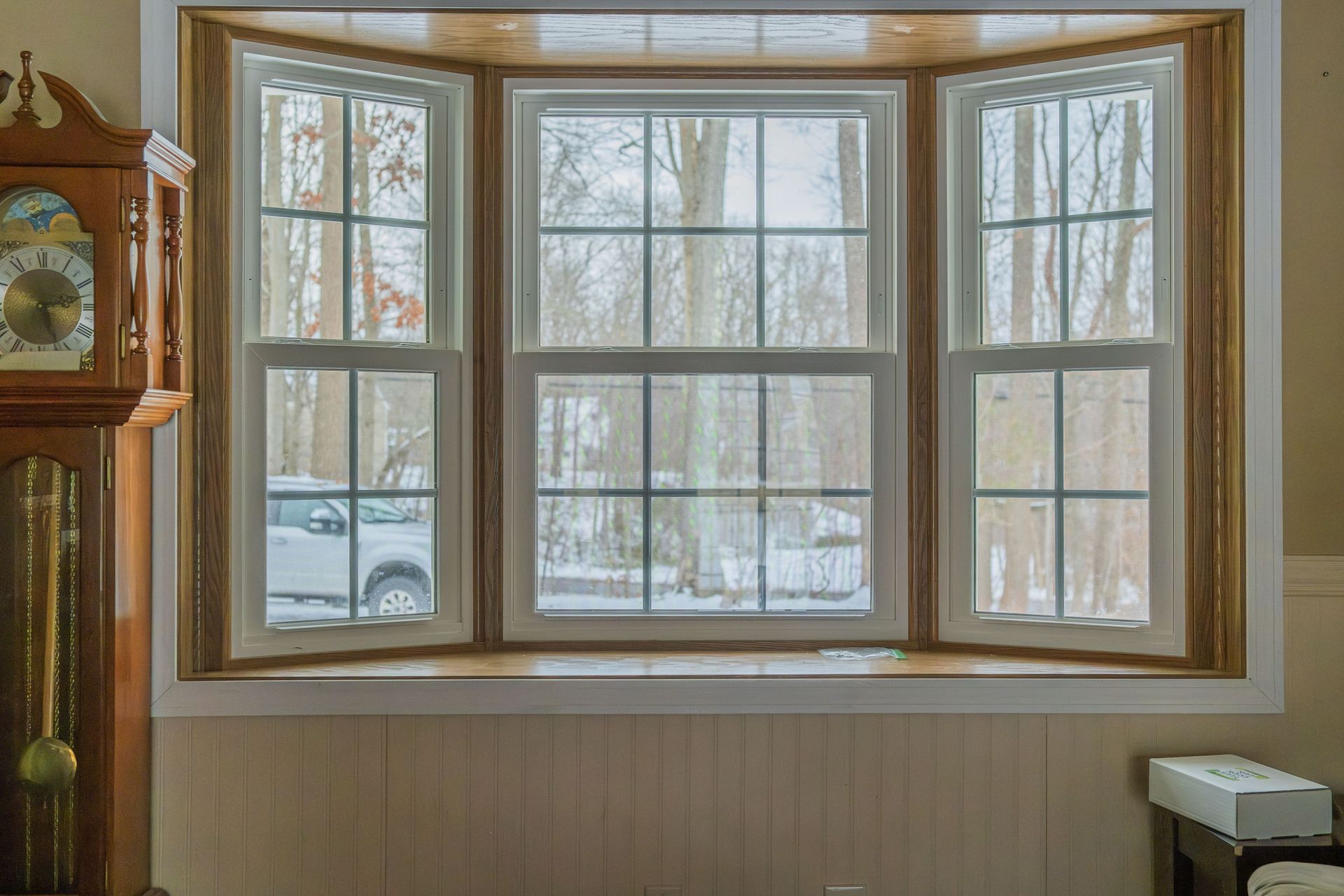 Bay window with three panes, white frames, wooden trim, and a snowy outdoor view.