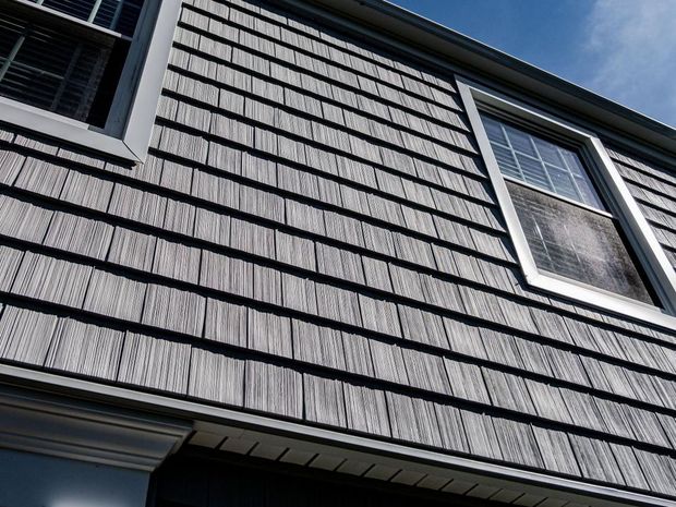 Gray shingle siding on a house with white-framed windows against a blue sky.