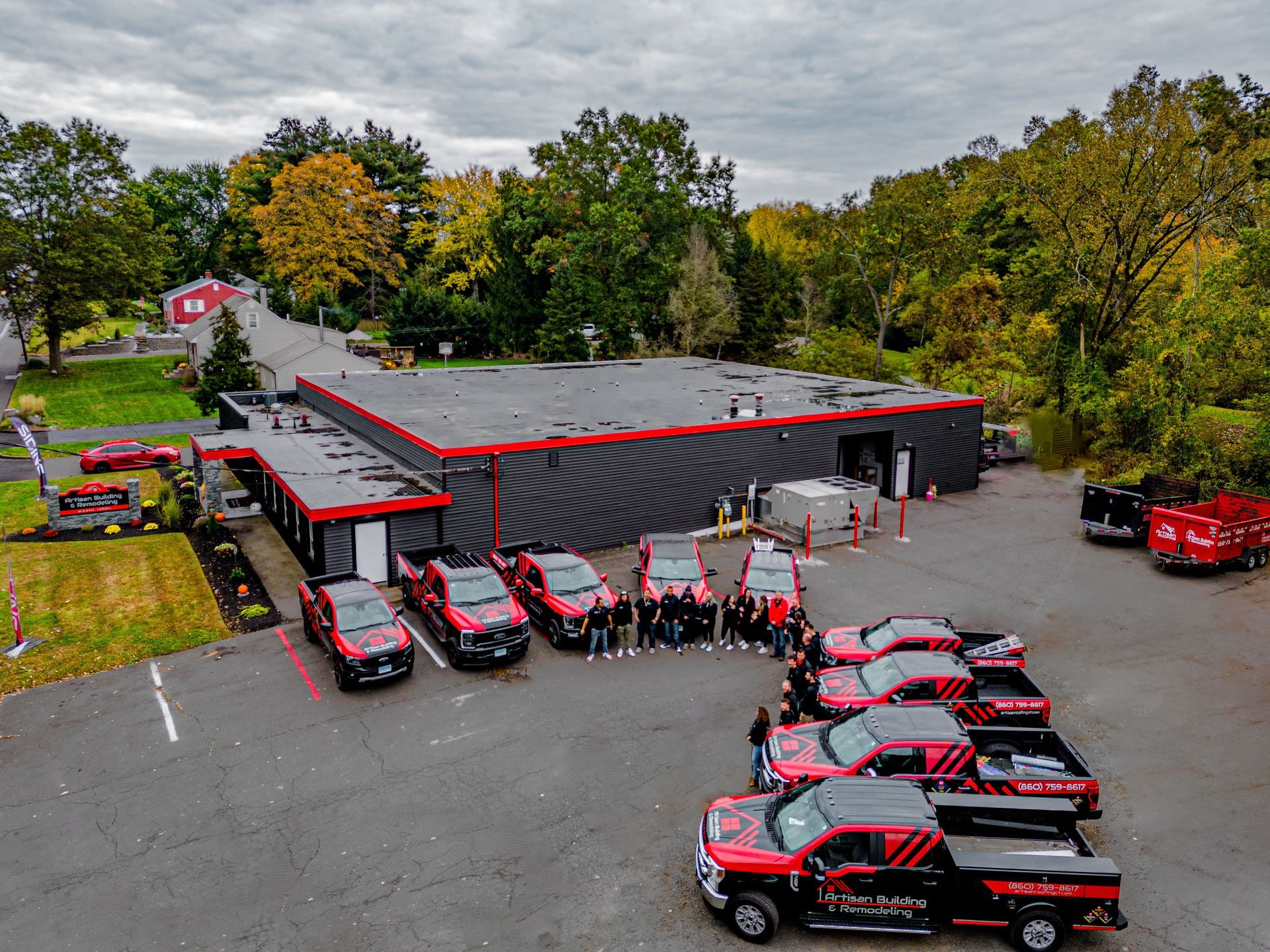 Group of people posing with red trucks in front of a building. Outdoors setting, overcast sky.