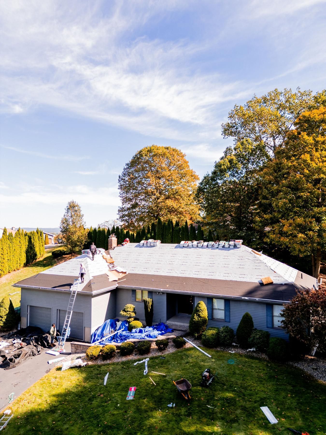 Workers replacing a roof on a gray house under a partly cloudy sky.