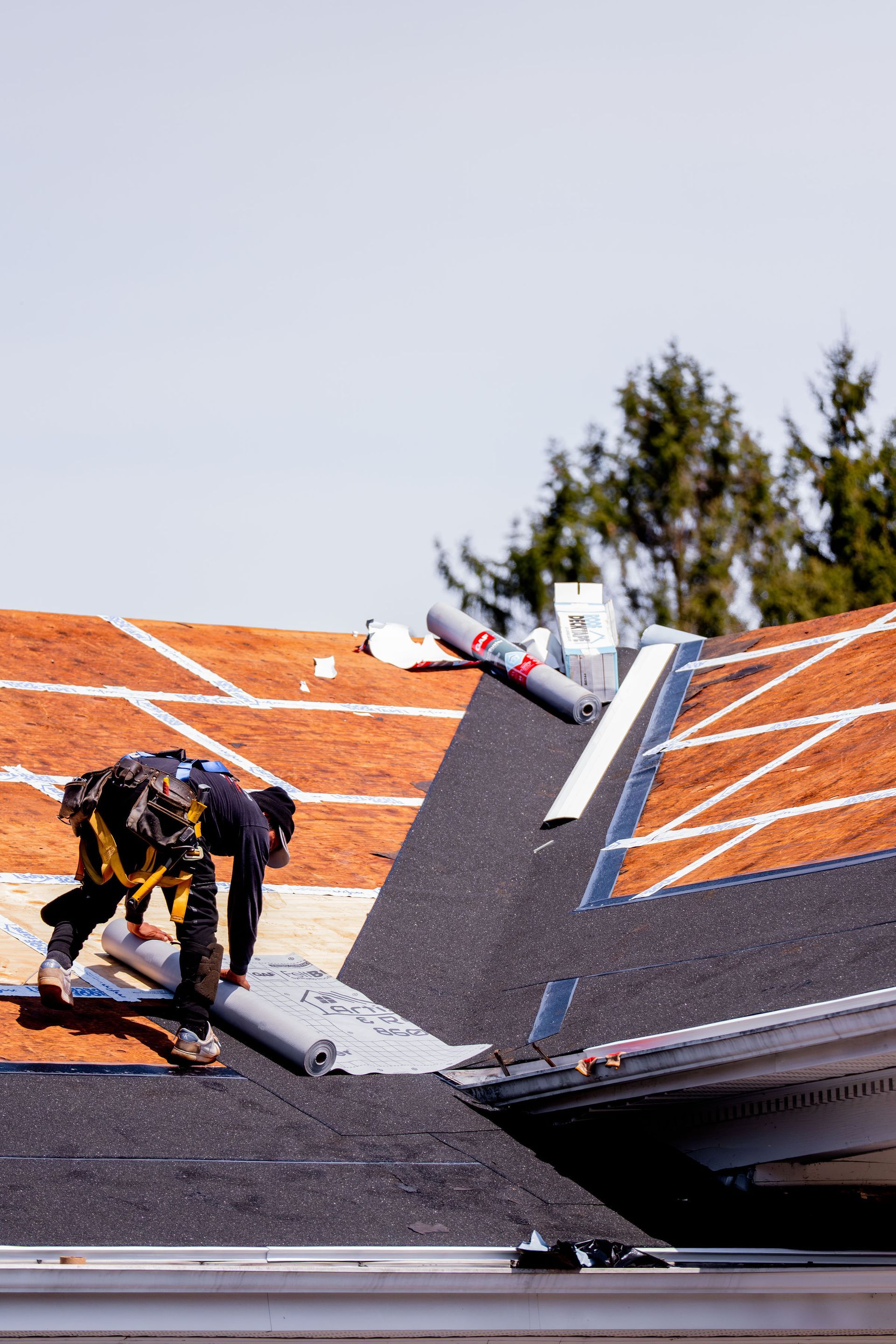 Roofer installs asphalt shingles on a partially completed roof on a sunny day.