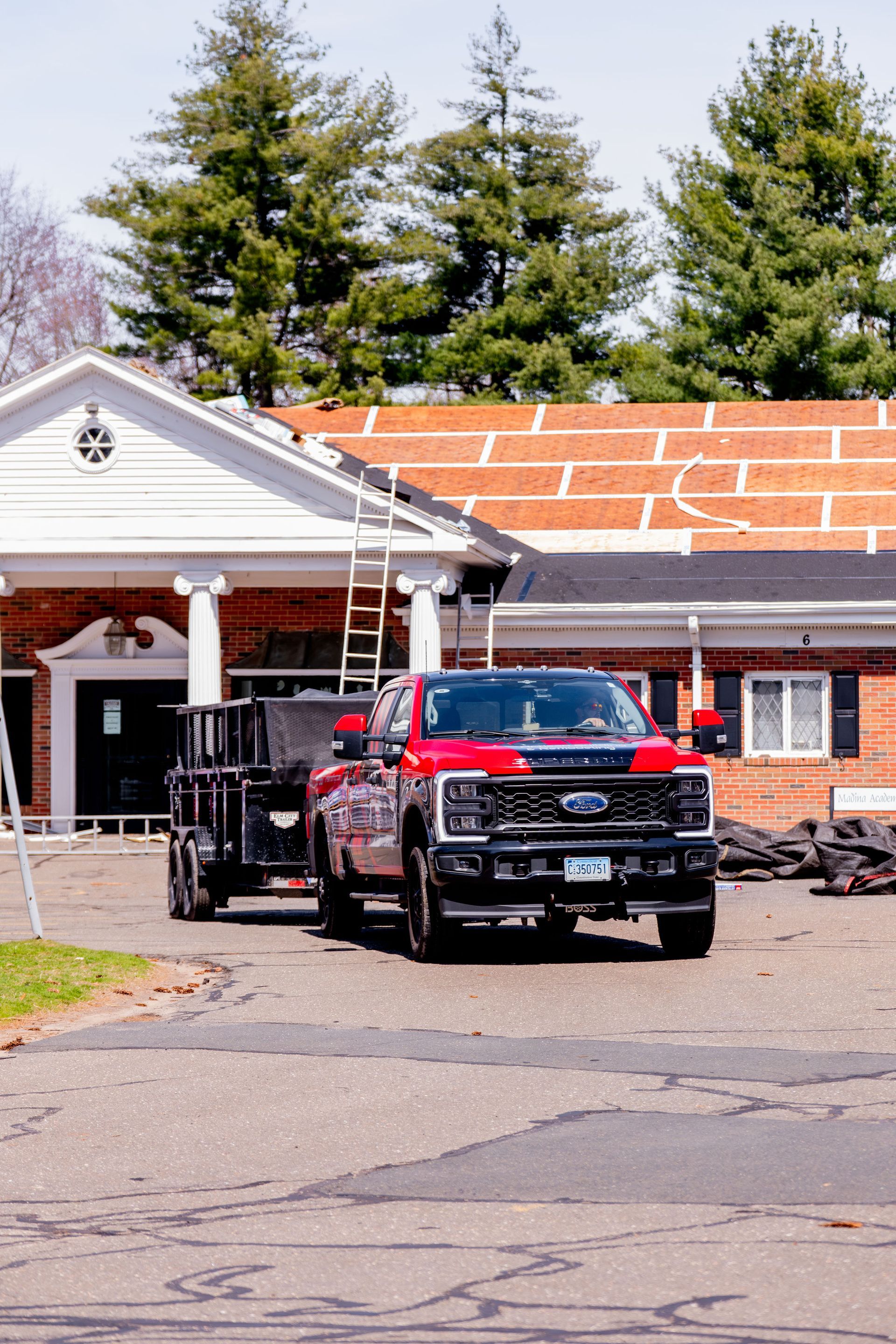 Red pickup truck with a trailer parked in front of a building with a roof under construction.