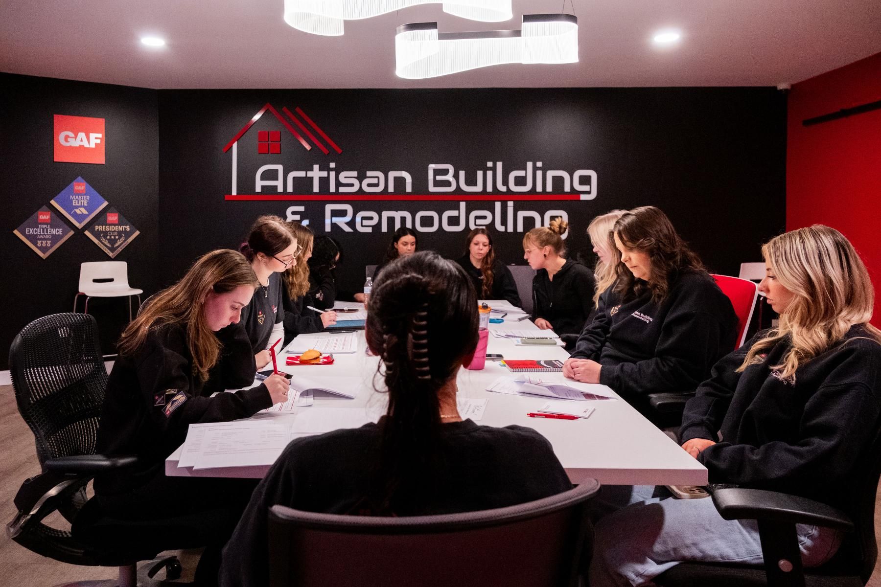 A team of people in a meeting room, looking at papers. The company logo is on the black wall.