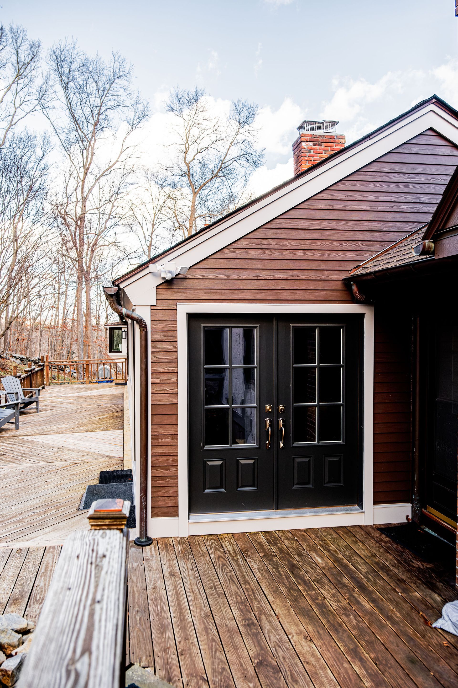 Brown house with black double doors on a wooden deck; bare trees in the background.