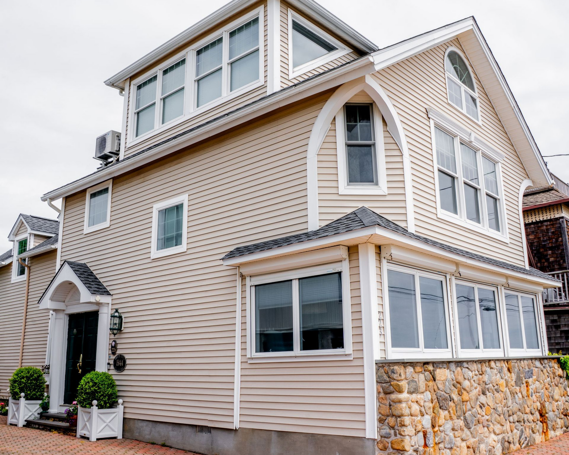 Three-story beige seaside house with white trim and stone foundation on a brick-paved street