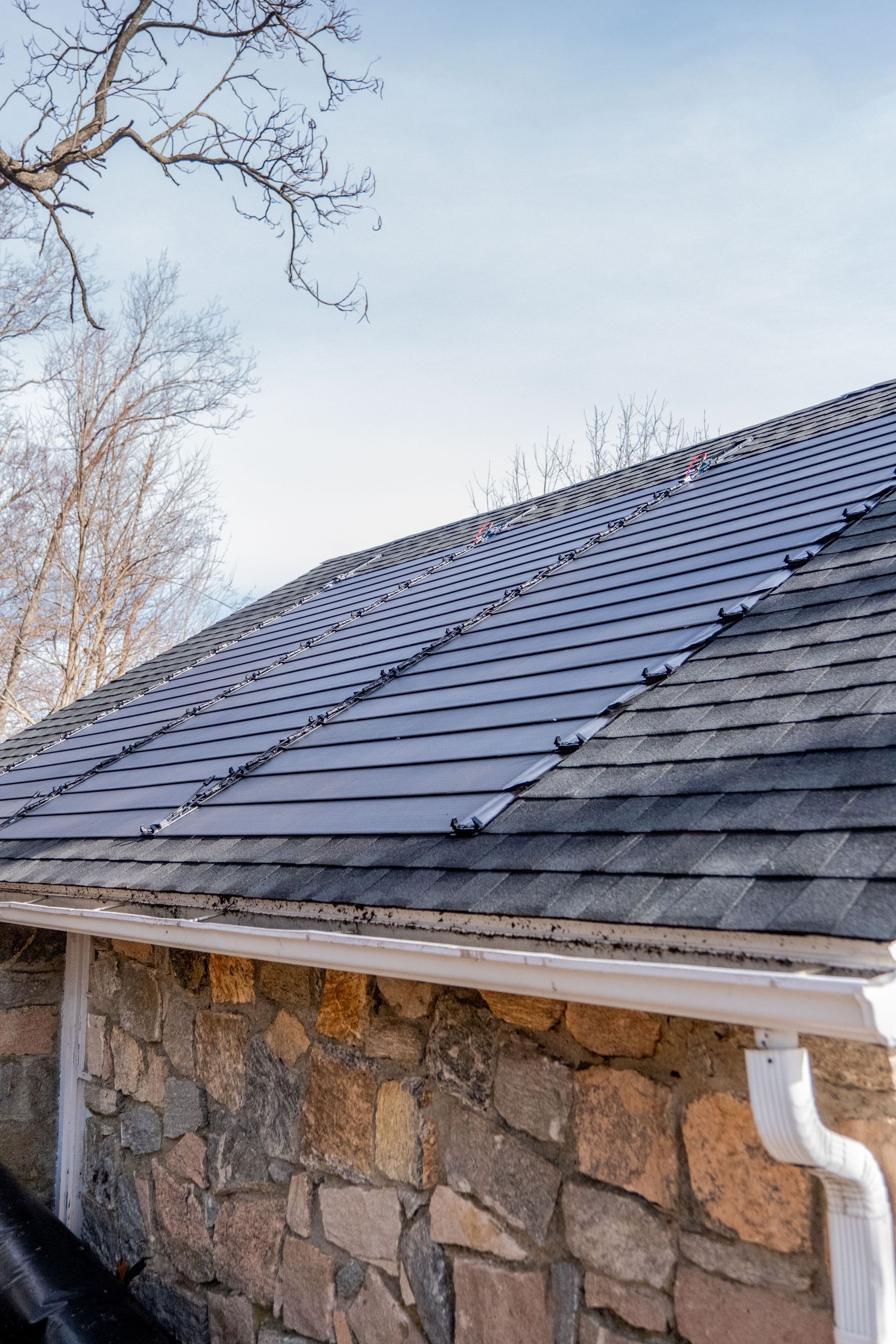 Stone house roof with dark shingles and white gutter under a pale sky