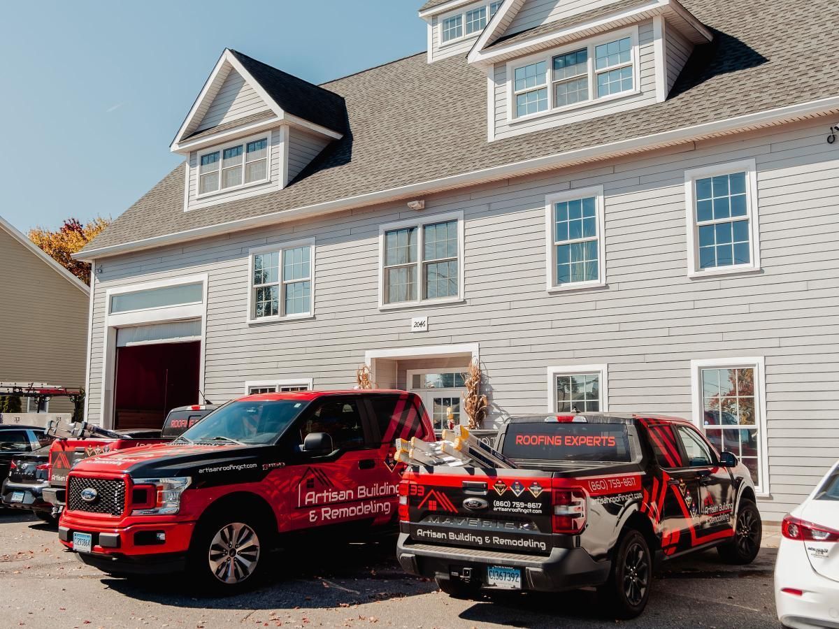 Two red pickup trucks parked in front of a gray two-story building. The trucks have company logos.