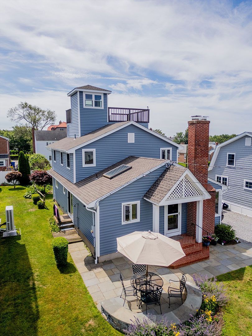Blue coastal home with tower, patio, and outdoor furniture under a sunny sky.