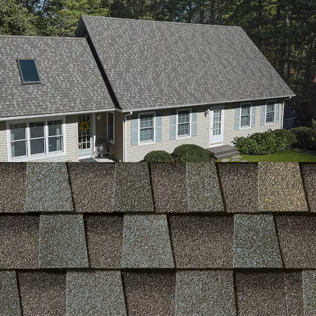Suburban house with gray roof seen behind a close-up of layered shingles in the foreground