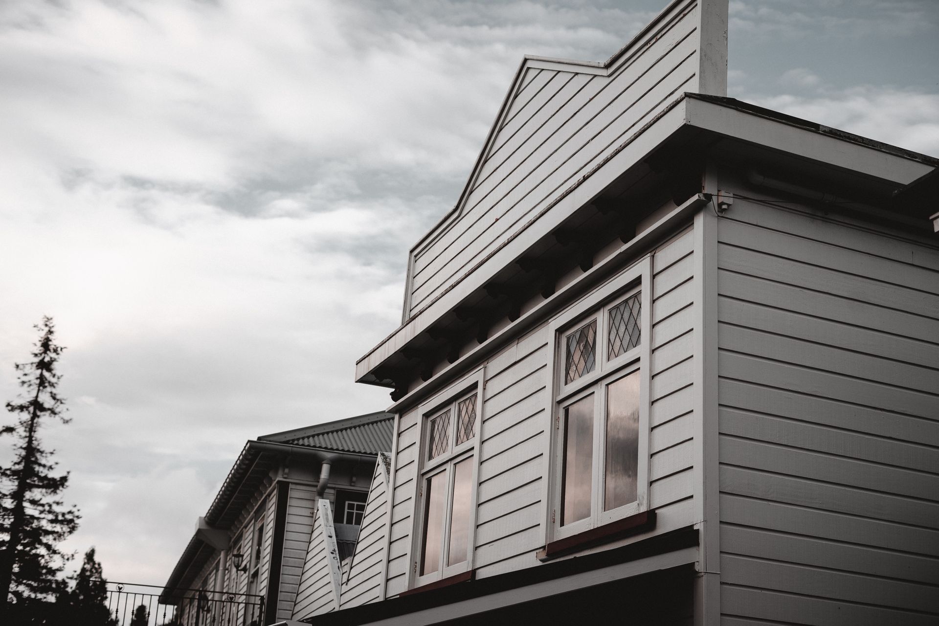Gray house exterior with gabled roof and windows under a cloudy sky