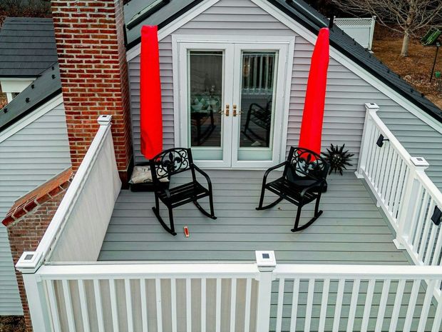 Rooftop deck with two black rocking chairs, French doors, red columns, white railing, and brick chimney.
