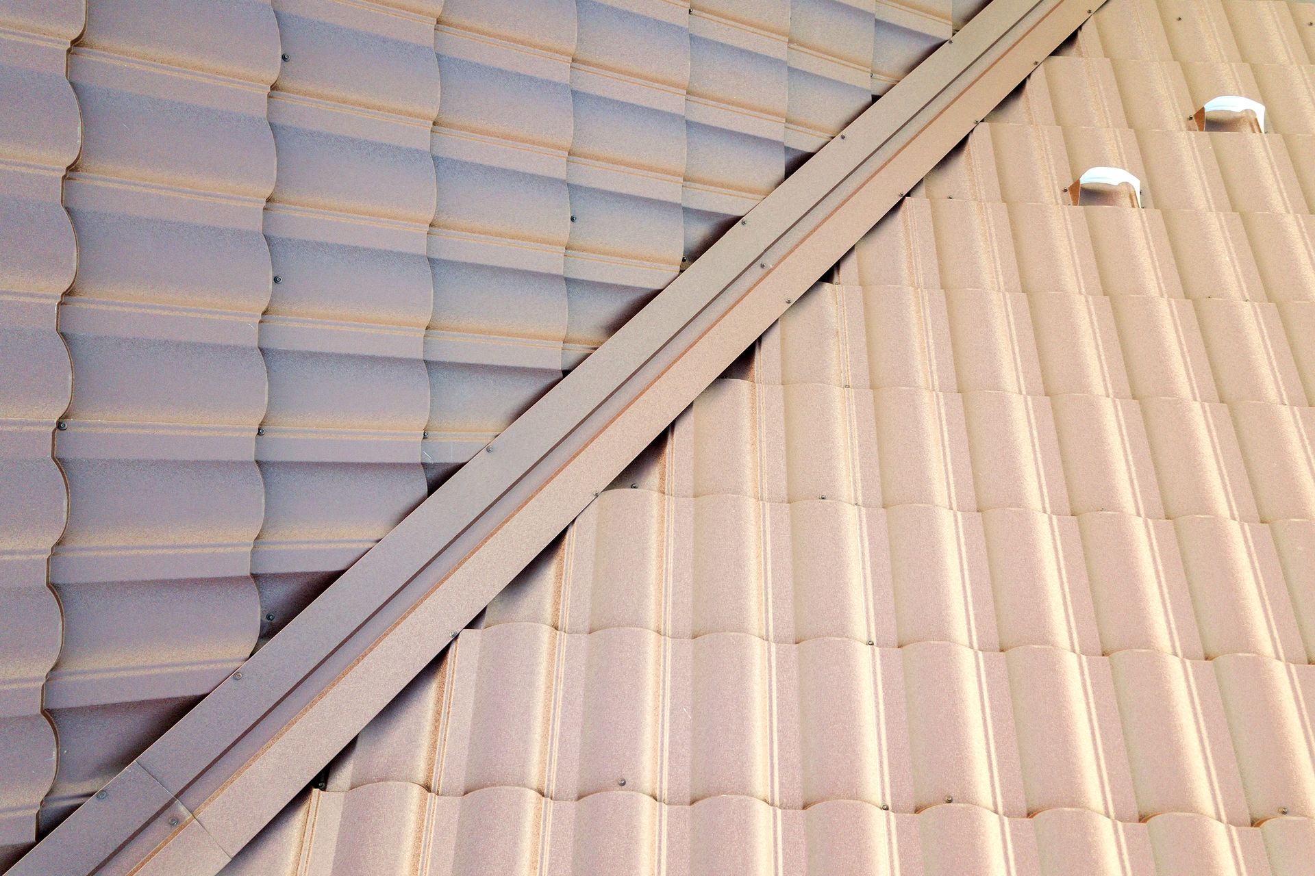 Diagonal ridge between two light-colored metal roofs with vents and matching panels