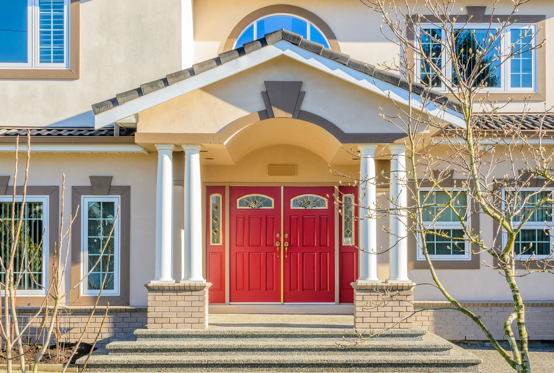 Front entrance of a beige house with red double doors, white columns, and steps leading up to the porch