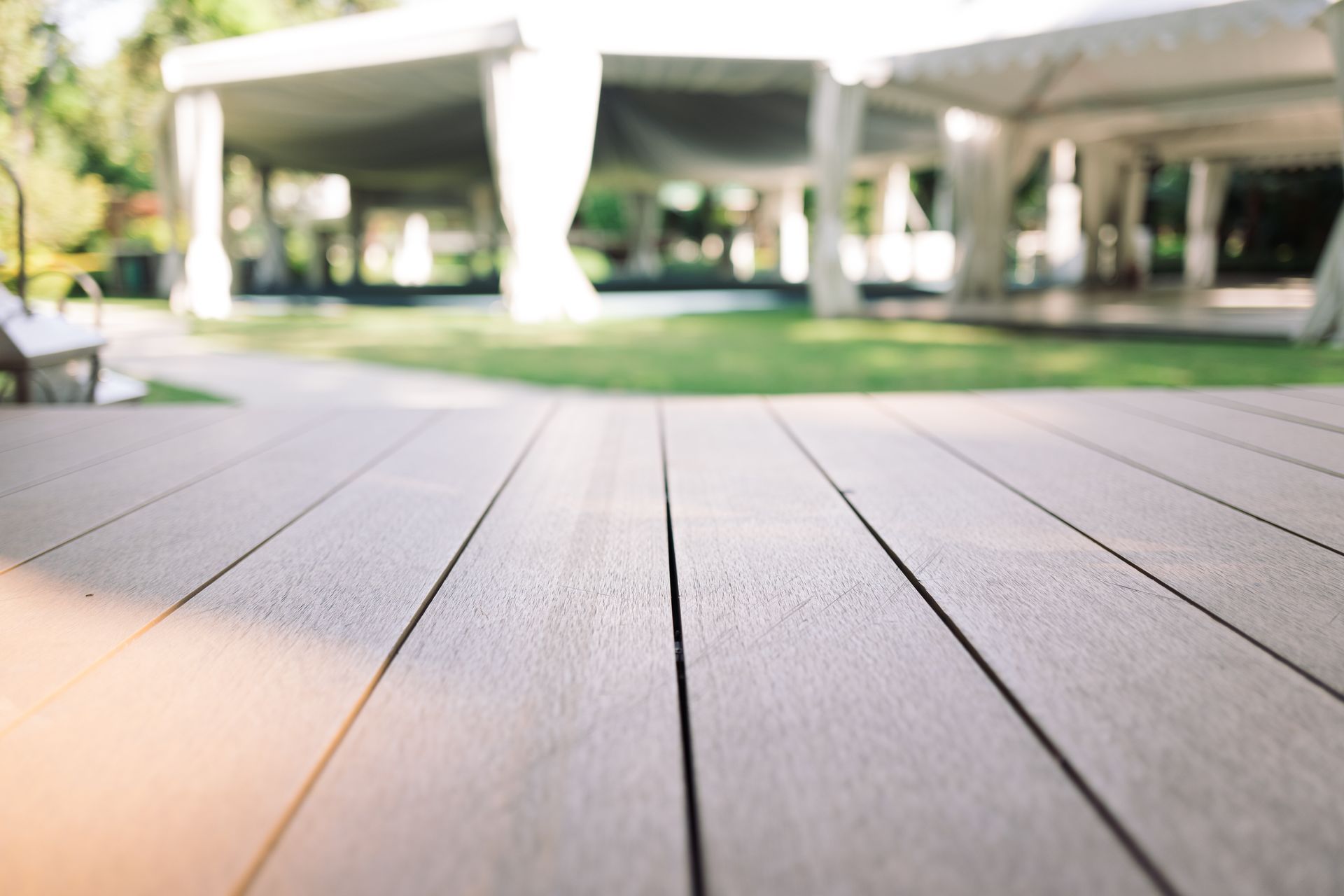 Empty wooden deck under a raised highway overpass, with sunlight and green grass beyond.