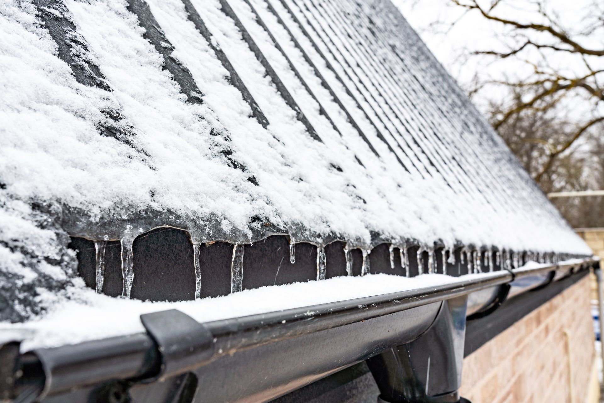 Snowy roof with icicles over a black gutter on a brick building, winter scene.