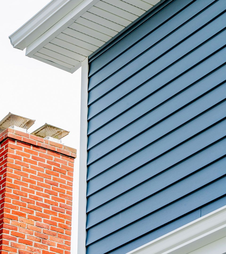Blue siding and white trim on a house, with a brick chimney.