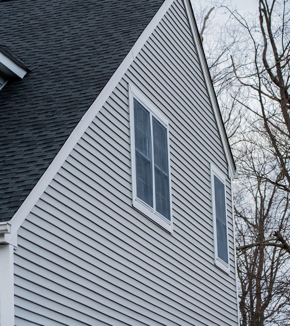 Gray siding on a house with two windows, white trim, and dark roof.