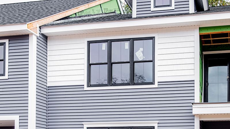 House under construction with gray and white siding, black window frames.