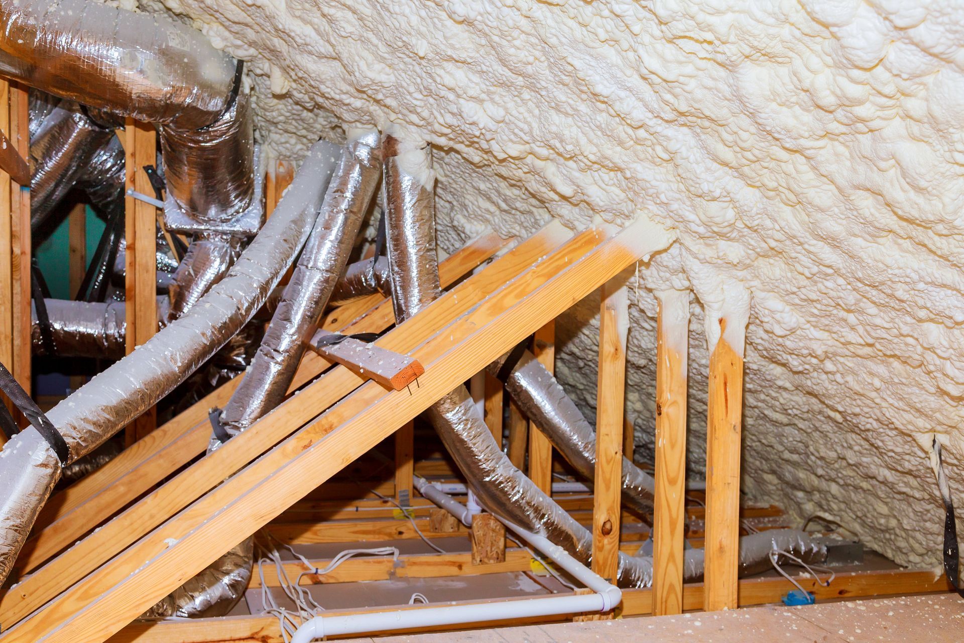 Attic with ductwork and spray foam insulation around wooden beams.