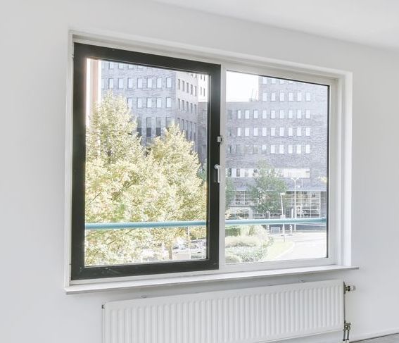 Window with black frame open to view of trees and buildings. White wall and radiator.