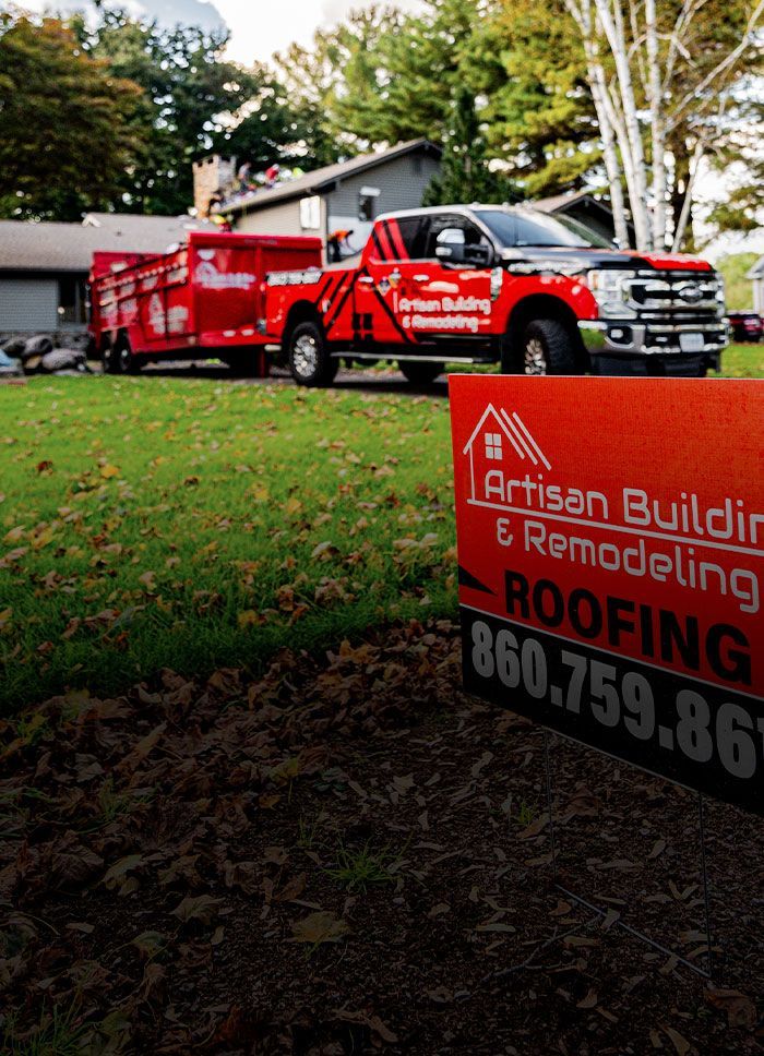 Red Artisan Building & Remodeling truck and trailer parked on a lawn, sign in foreground.