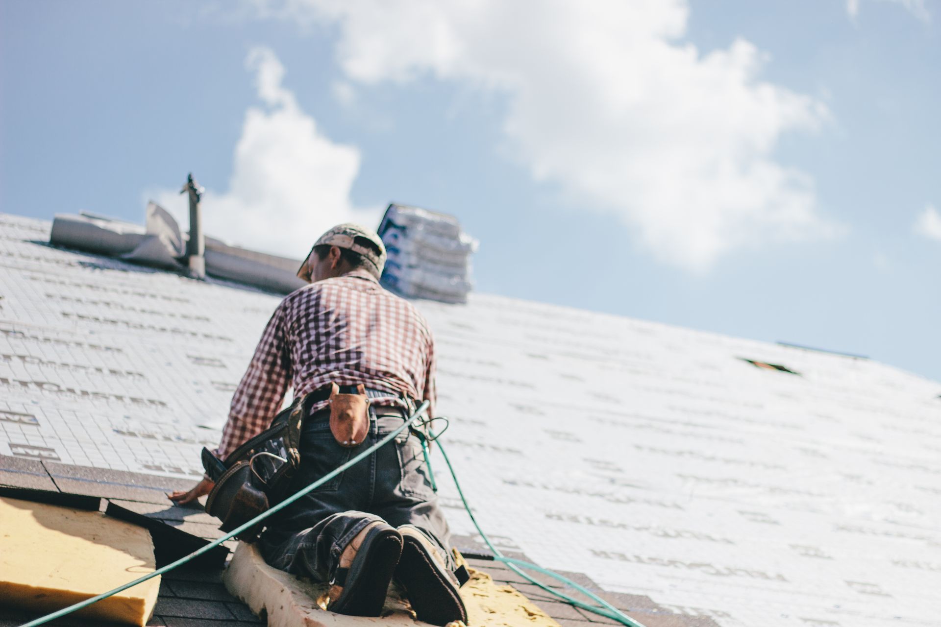 Worker on a rooftop installing shingles near a chimney on a clear day