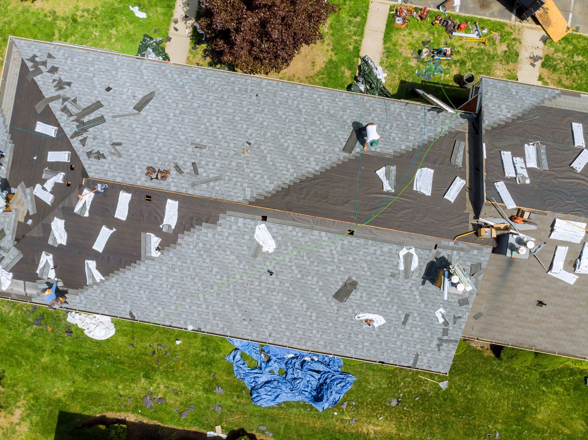 An aerial view shows a residential roof undergoing repair, with partially replaced shingles and scattered construction debris.