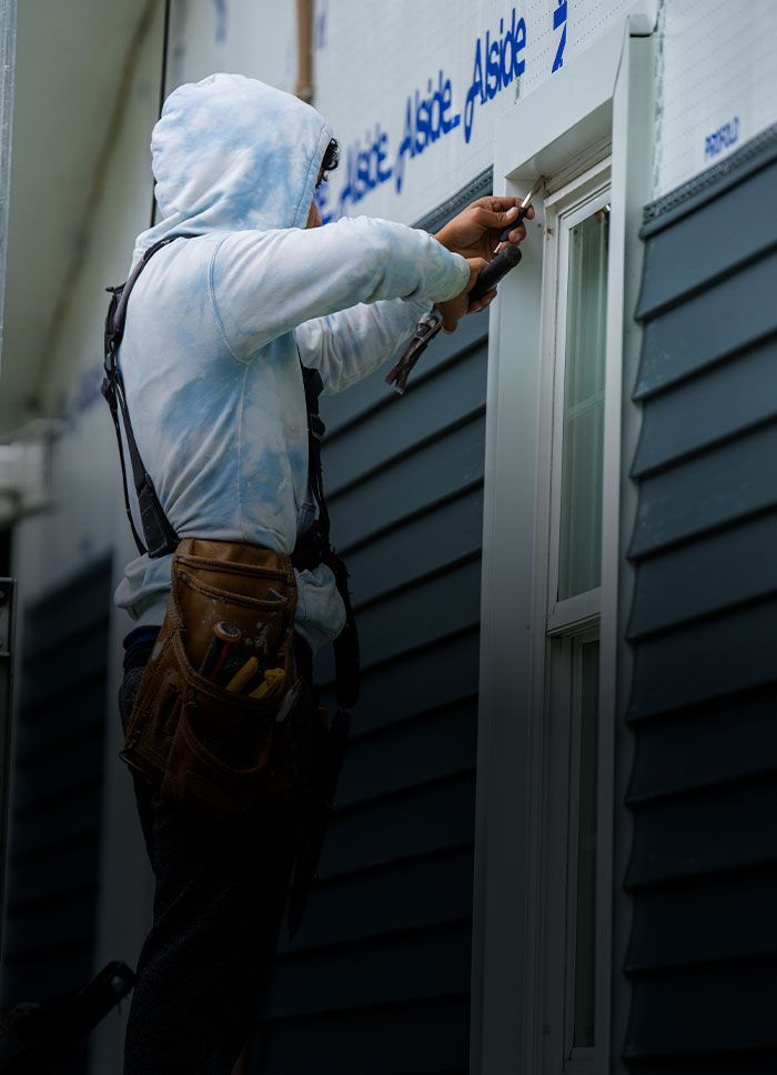 Construction worker installing window trim on a blue siding house.