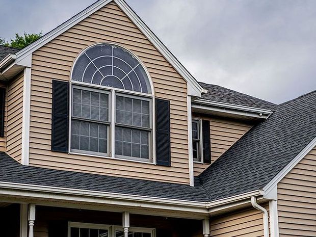 Beige house with a dark gray roof, black shutters, and an arched window.