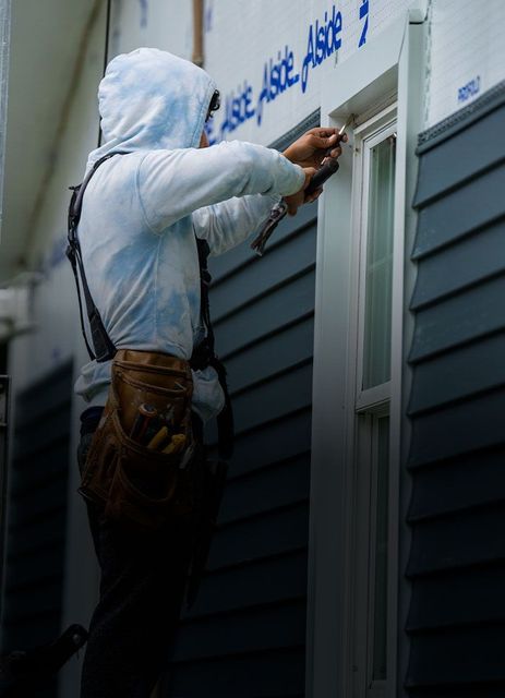 Construction worker installing window trim on a blue siding house.