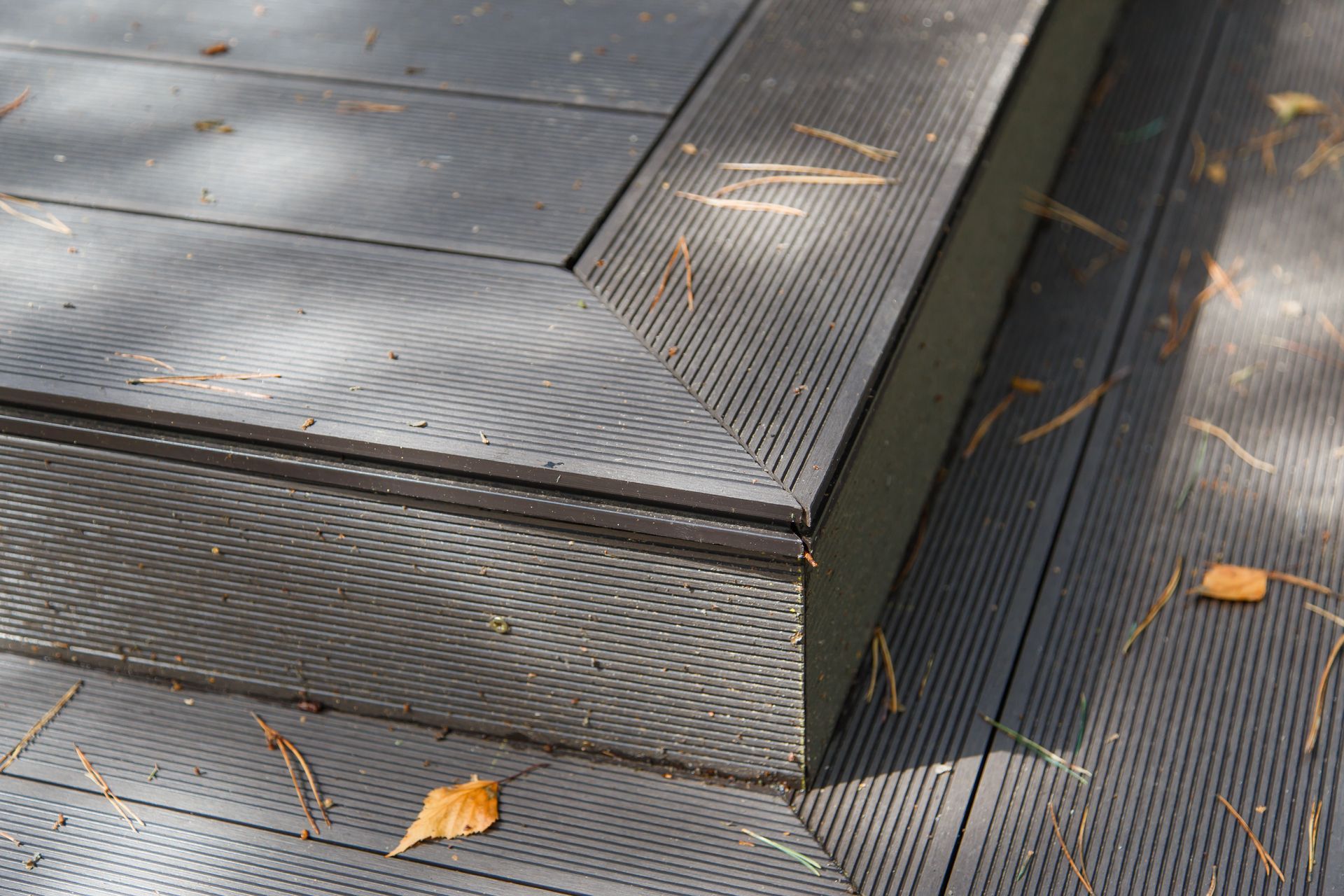 Close-up of textured dark gray metal steps with scattered orange leaves outdoors