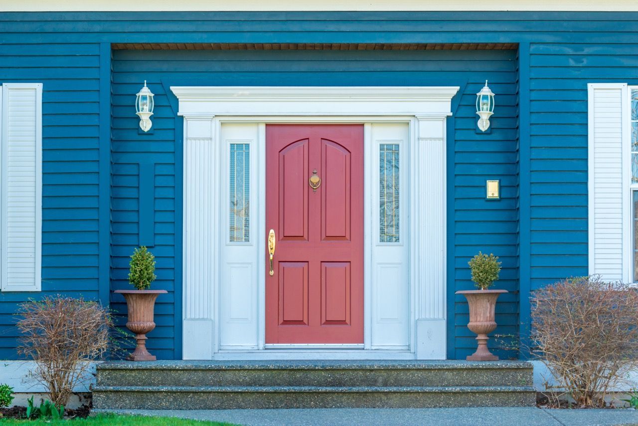 Blue house facade with a pink front door, white trim, and potted plants by the steps