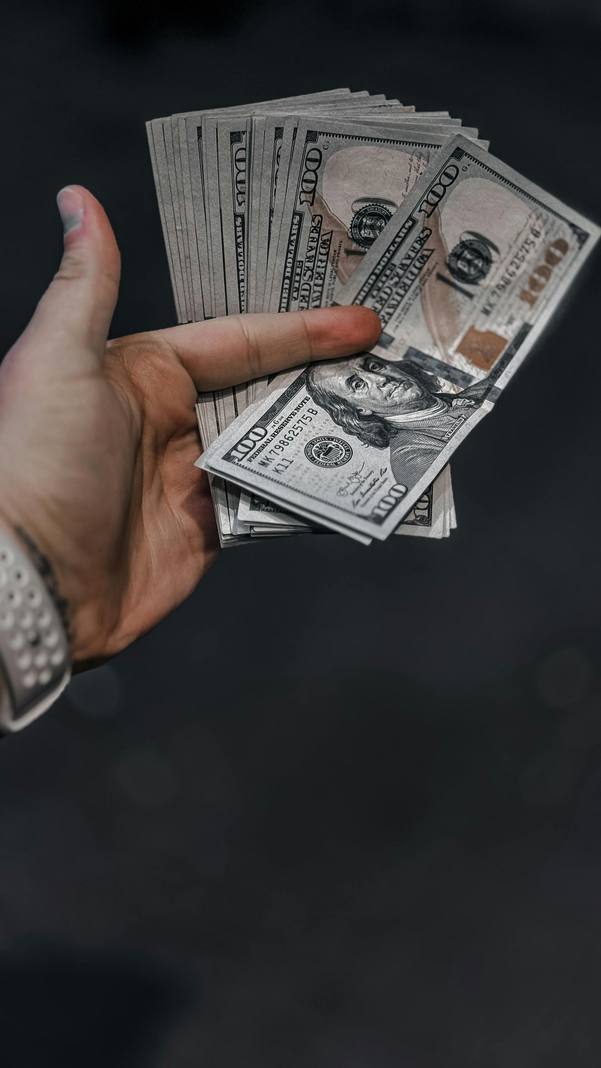 Hand holding several U.S. dollar bills against a dark background