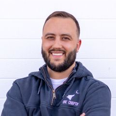 Smiling bearded man in a navy hoodie standing against a white wall