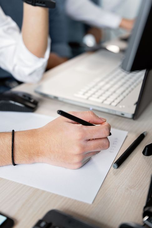 Hand writing notes beside a laptop on a desk