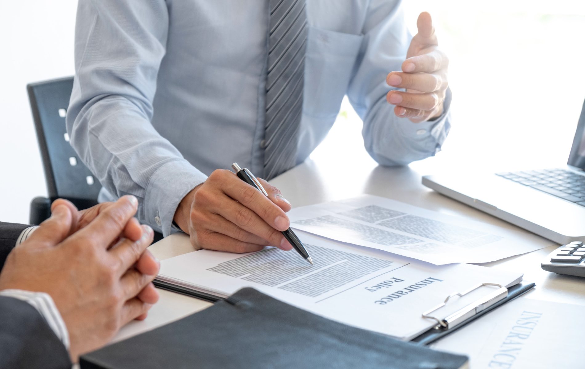 People in business attire discussing documents at a desk with a clipboard and laptop