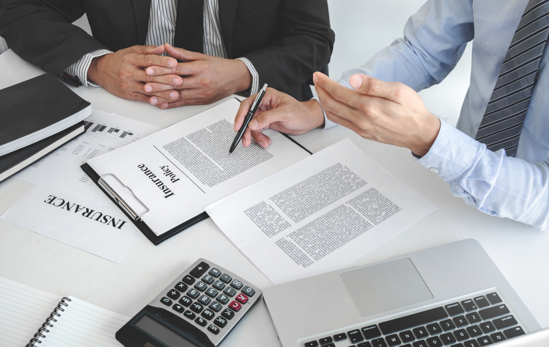 Business meeting with hands over documents, calculator, and laptop on a desk